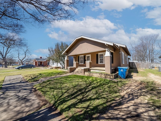 view of front of house featuring a porch, a front lawn, fence, and brick siding