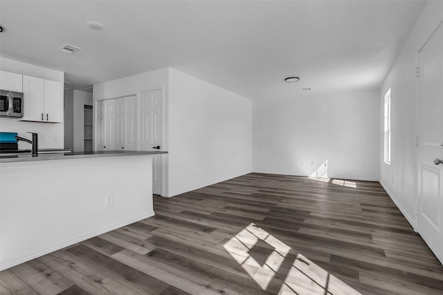 unfurnished living room featuring dark wood-style floors, visible vents, and a sink