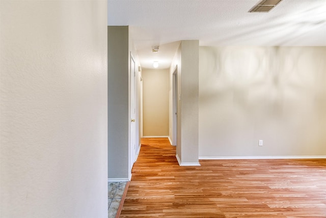 hall featuring a textured ceiling, light wood-type flooring, visible vents, and baseboards