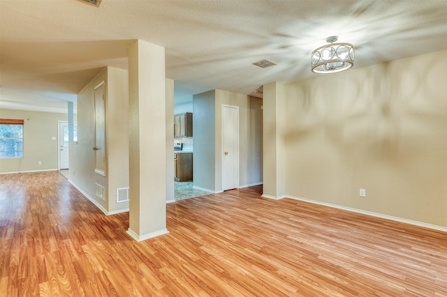 empty room with light wood finished floors, visible vents, and baseboards