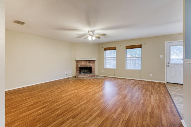 unfurnished living room with visible vents, baseboards, light wood-style flooring, ceiling fan, and a brick fireplace