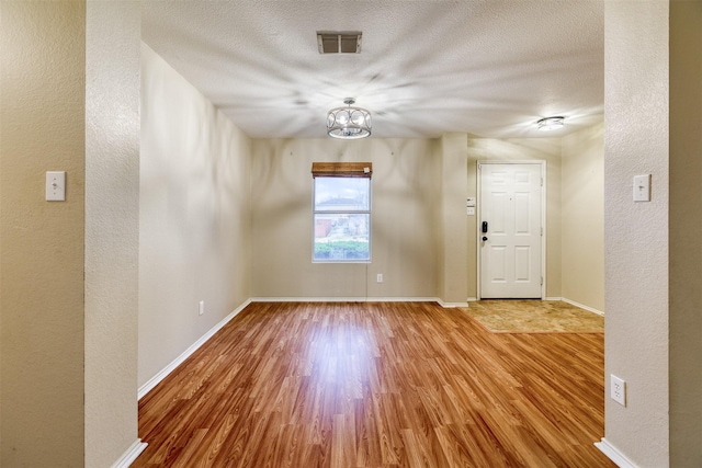 foyer featuring baseboards, a textured ceiling, visible vents, and wood finished floors