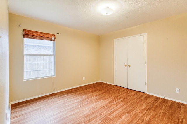 unfurnished bedroom with light wood-style floors, a closet, a textured ceiling, and baseboards