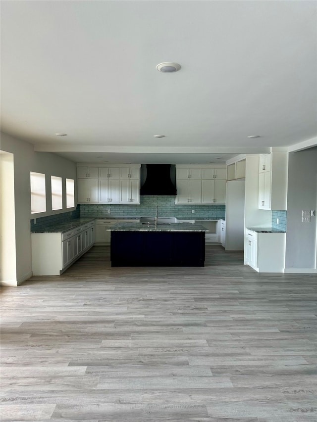 kitchen with a center island, light wood-style flooring, decorative backsplash, a sink, and wall chimney exhaust hood