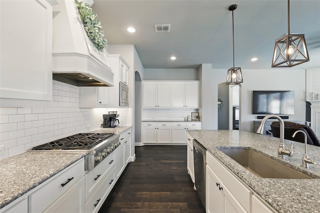 kitchen featuring dark wood finished floors, decorative light fixtures, custom range hood, stainless steel appliances, and a sink