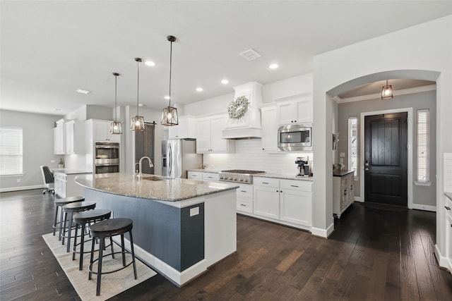 kitchen with premium range hood, an island with sink, a sink, stainless steel appliances, and backsplash