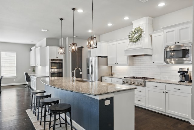 kitchen featuring premium range hood, a center island with sink, a sink, backsplash, and stainless steel appliances