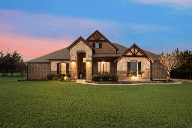 view of front of home with a shingled roof, stone siding, brick siding, and a yard