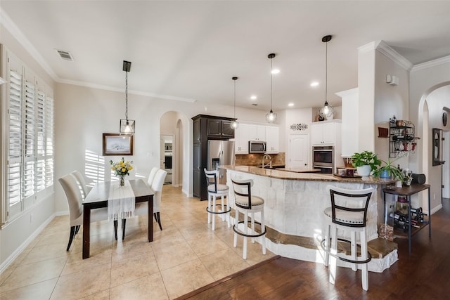 kitchen featuring arched walkways, stainless steel appliances, a breakfast bar area, and crown molding