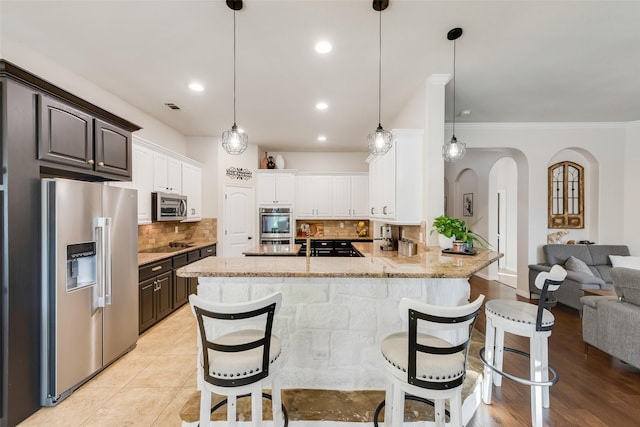 kitchen featuring light stone counters, arched walkways, stainless steel appliances, visible vents, and decorative backsplash