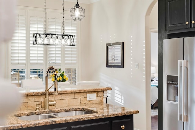 kitchen featuring arched walkways, a sink, light stone countertops, dark cabinets, and stainless steel fridge with ice dispenser