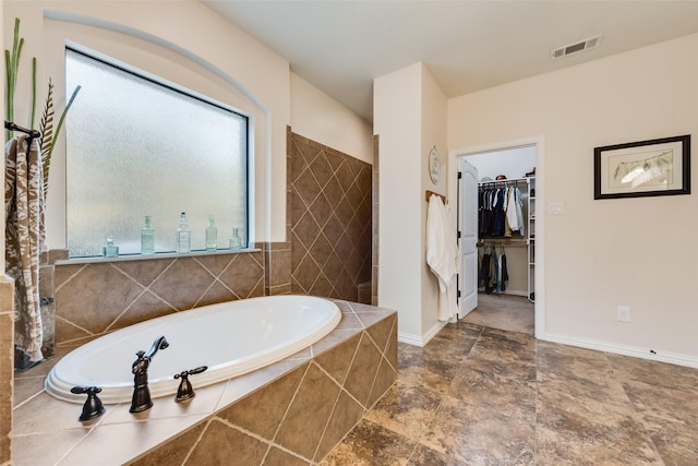 full bathroom featuring a walk in closet, visible vents, a garden tub, and tiled shower