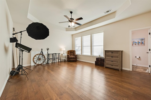 living area featuring baseboards, visible vents, a ceiling fan, wood finished floors, and a tray ceiling