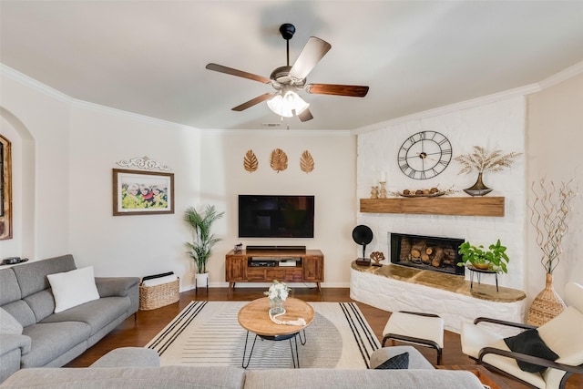 living area with a large fireplace, wood finished floors, visible vents, a ceiling fan, and ornamental molding