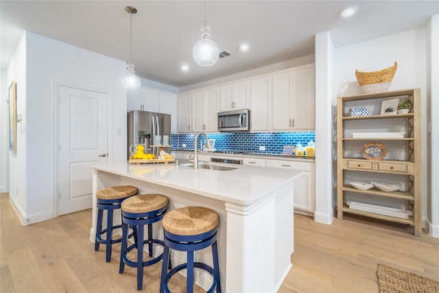 kitchen with a breakfast bar area, decorative backsplash, appliances with stainless steel finishes, a sink, and light wood-type flooring