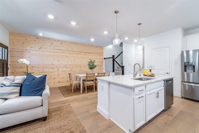 kitchen with light wood finished floors, open floor plan, stainless steel appliances, wood walls, and a sink