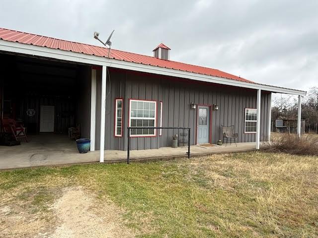 back of house featuring a patio area, a lawn, metal roof, and board and batten siding