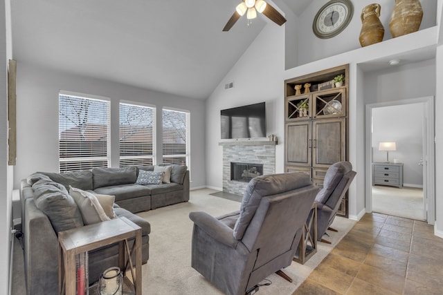 carpeted living room with visible vents, a ceiling fan, a stone fireplace, high vaulted ceiling, and baseboards