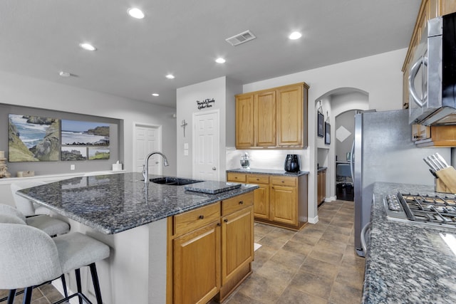 kitchen with arched walkways, a center island with sink, a breakfast bar area, appliances with stainless steel finishes, and a sink