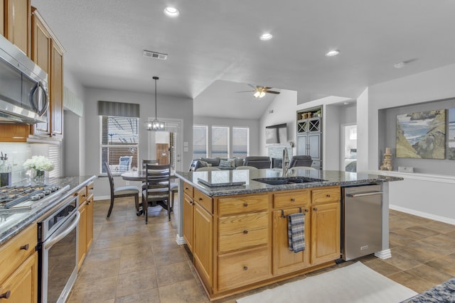 kitchen featuring ceiling fan with notable chandelier, a sink, appliances with stainless steel finishes, dark stone counters, and plenty of natural light