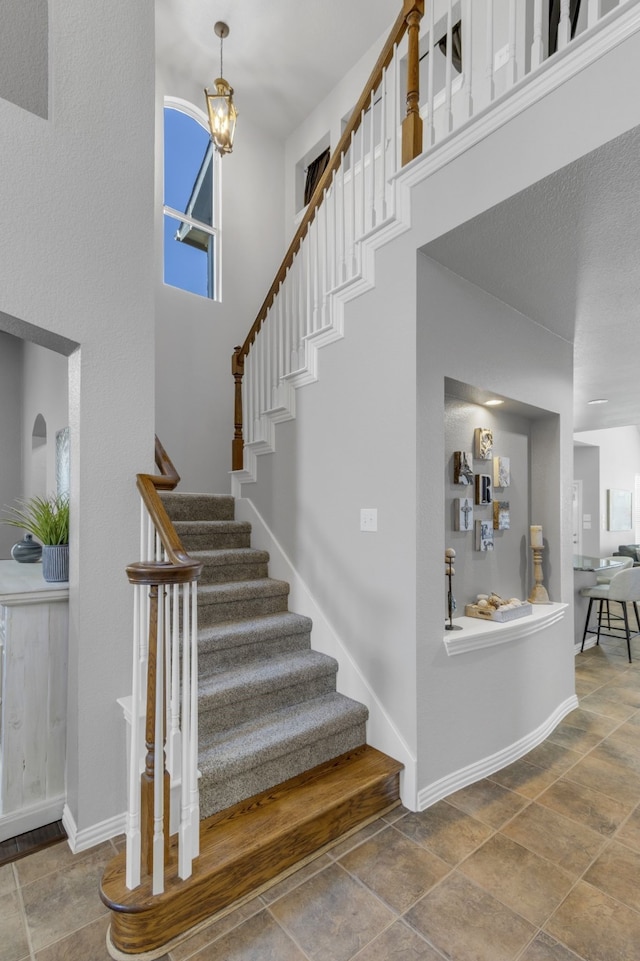 stairway featuring a towering ceiling, stone finish floor, and baseboards