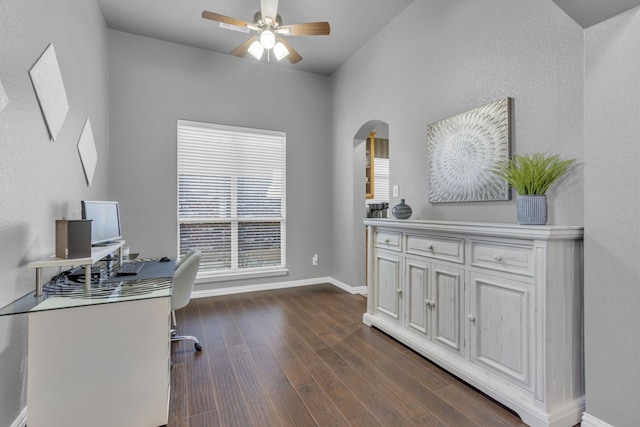 home office featuring dark wood-style floors, arched walkways, ceiling fan, and baseboards