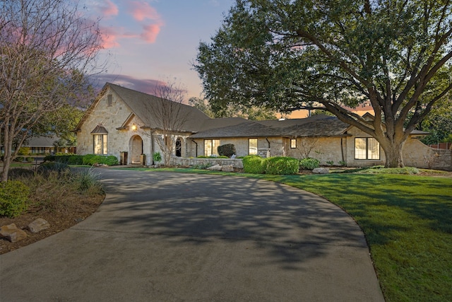 french country inspired facade featuring driveway, stone siding, and a front lawn