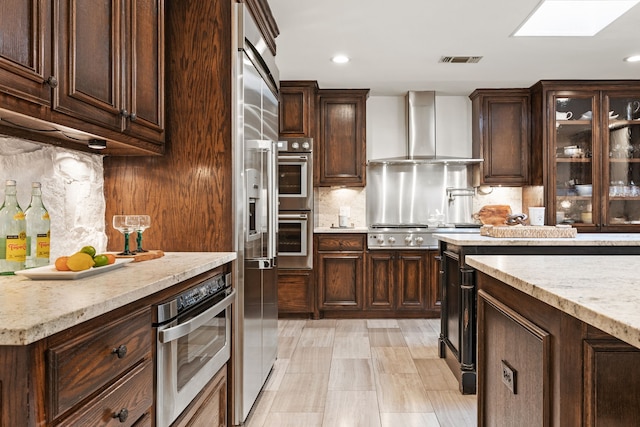 kitchen featuring stainless steel appliances, visible vents, dark brown cabinets, backsplash, and wall chimney exhaust hood