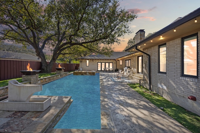 pool at dusk featuring a fire pit, a patio area, a fenced backyard, and a fenced in pool