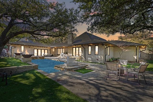 back of house at dusk with a patio, brick siding, a yard, crawl space, and a chimney