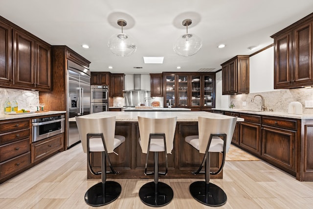 kitchen featuring wall chimney exhaust hood, dark brown cabinets, a sink, and appliances with stainless steel finishes