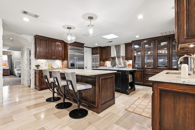 kitchen with visible vents, a kitchen island, appliances with stainless steel finishes, wall chimney range hood, and a sink