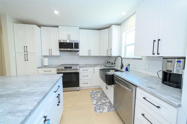 kitchen with stainless steel appliances, a sink, white cabinets, backsplash, and light stone countertops