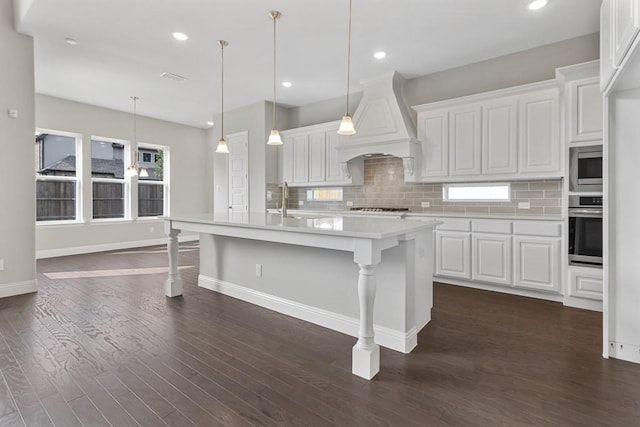 kitchen featuring appliances with stainless steel finishes, light countertops, premium range hood, white cabinetry, and backsplash