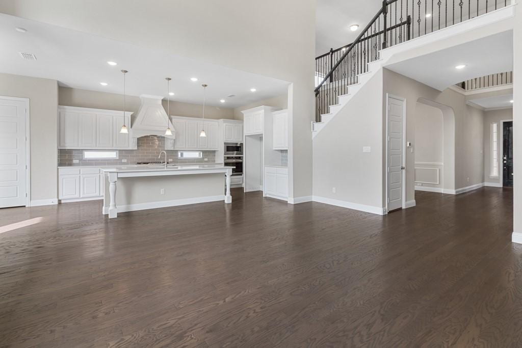 unfurnished living room with recessed lighting, a sink, dark wood finished floors, and baseboards