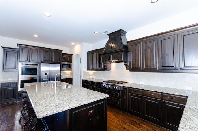 kitchen featuring arched walkways, stainless steel appliances, a sink, decorative backsplash, and custom range hood