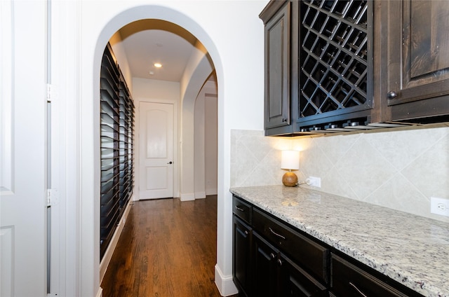 interior space featuring a dry bar, baseboards, arched walkways, decorative backsplash, and dark wood-style flooring