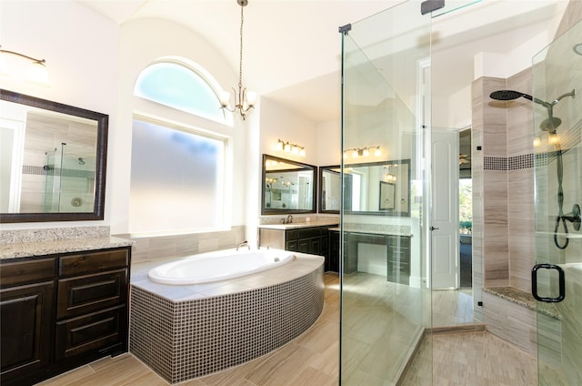 bathroom with a stall shower, vanity, a bath, and a notable chandelier