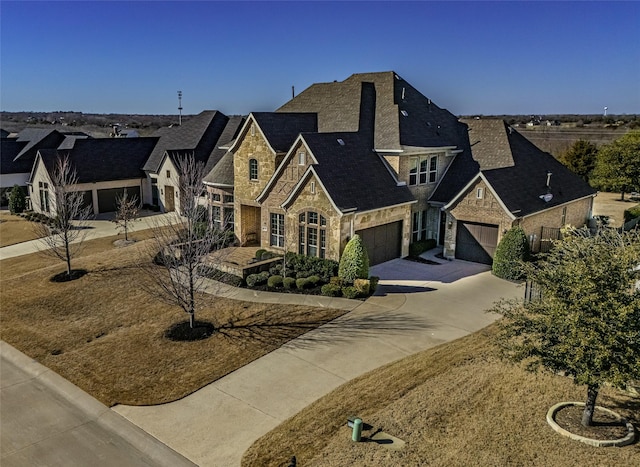 french provincial home with stone siding, an attached garage, and driveway