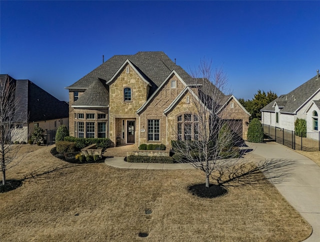 french country home with stone siding, brick siding, concrete driveway, and fence