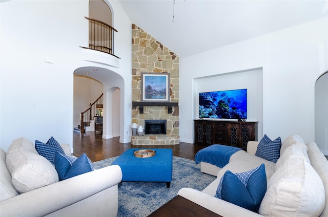 living room featuring arched walkways, a stone fireplace, stairway, and wood finished floors