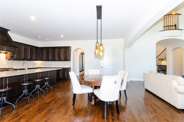 dining space featuring arched walkways, dark wood finished floors, and recessed lighting