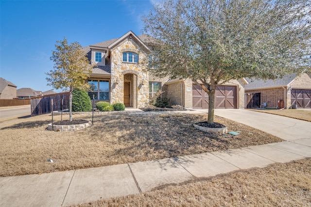 view of front of house featuring stone siding, driveway, and fence