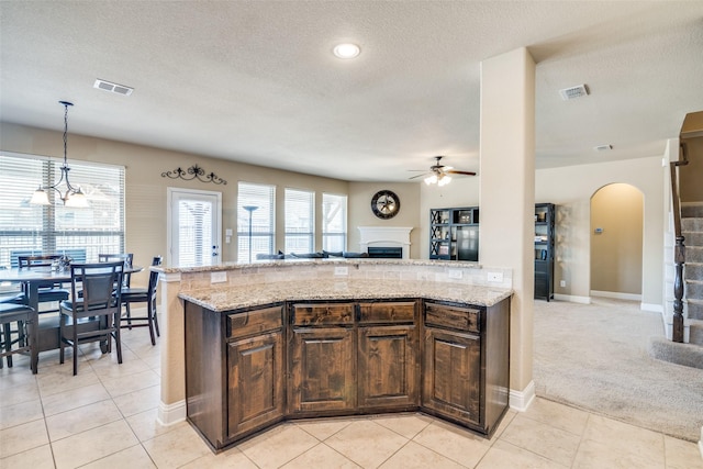 kitchen with dark brown cabinets, light stone counters, a fireplace, and visible vents