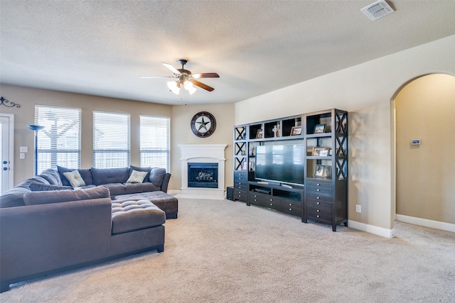 carpeted living area with arched walkways, a fireplace, visible vents, ceiling fan, and baseboards