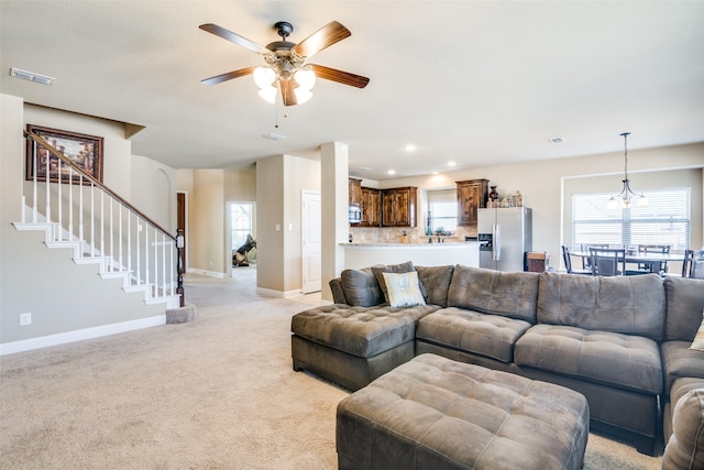 living area with ceiling fan, light colored carpet, visible vents, baseboards, and stairs