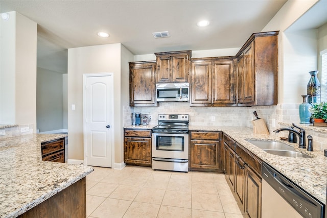 kitchen featuring stainless steel appliances, tasteful backsplash, a sink, and light stone counters