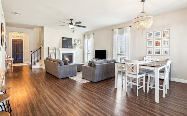 living area with baseboards, visible vents, a glass covered fireplace, wood finished floors, and ceiling fan with notable chandelier