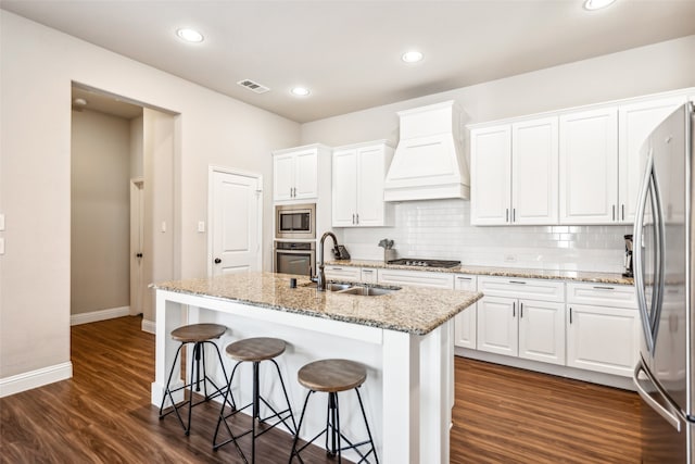 kitchen with decorative backsplash, custom range hood, stainless steel appliances, white cabinetry, and a sink