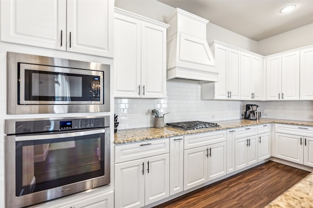 kitchen with stainless steel appliances, premium range hood, decorative backsplash, and white cabinetry